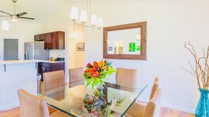 Een eethoek met een glazen tafel en geweven stoelen, een keuken achtergrond en een spiegel aan de muur.
