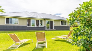 Een modern gebouw met een plat dak en grote ramen. Drie lounge fauteuils staan op een gazon voor het gebouw.