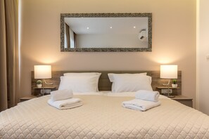 Una habitación de hotel con una cama grande, dos lámparas de noche, un espejo y una pequeña planta en maceta.