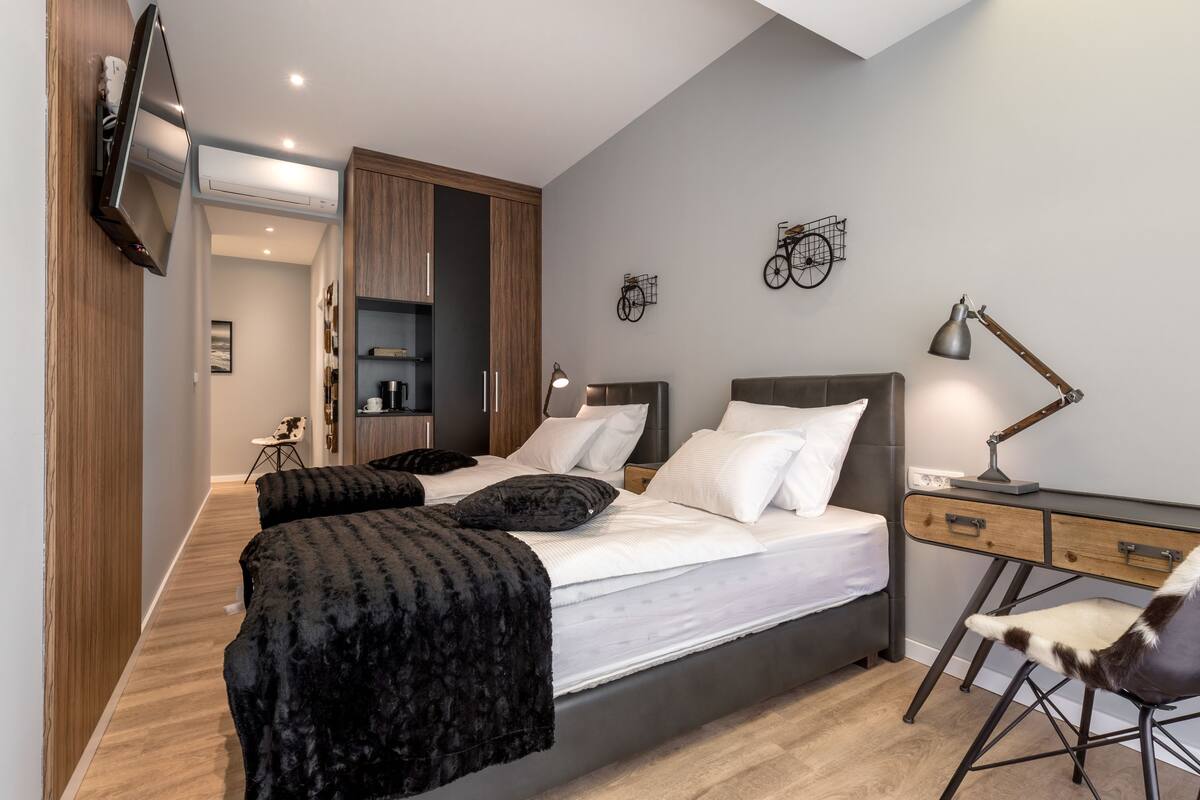 A modern bedroom with a large bed, a desk, and a chair. There is a TV mounted on the wall and a bicycle decoration on the wall.