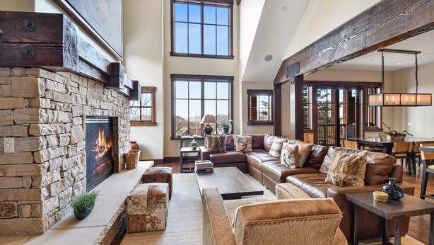 A spacious living room with a stone fireplace, large windows, a leather sofa, and a dining area. - Silver Star 47 | Resort Amenities (Park City)