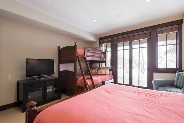 A bedroom with a bunk bed, a television on a cabinet, and a window with a view of trees.