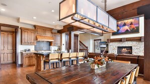 A spacious kitchen with wooden cabinets, a central island with chairs, a hanging light fixture, and a stone fireplace. - Silver Star 47 | Resort Amenities (Park City)