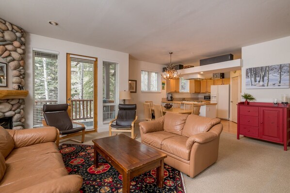 A spacious living area with a fireplace, leather sofas, and a dining area with a kitchen in the background.