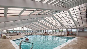Ein Hallenbad mit hoher Decke und Dachfenstern, umgeben von Liegestühlen und einem Betonboden.