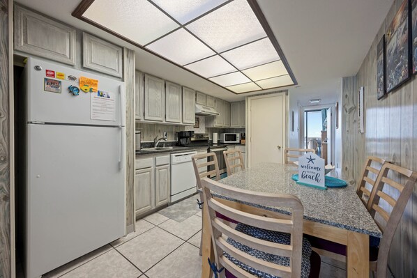 A kitchen with white cabinets, a refrigerator, a microwave, and a dining table with chairs.