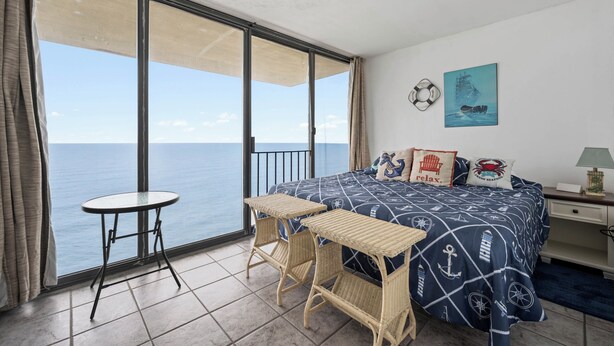 Ein Balkon mit Meerblick, ein Bett mit maritimer Bettwäsche und ein kleiner Tisch.
