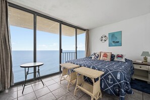 A balcony with a view of the sea, a bed with nautical-themed bedding, and a small table.