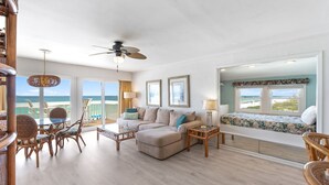 Amplia sala de estar con un gran ventanal con vista al mar, un sofá cómodo, una mesa de comedor con sillas y una pequeña zona de balcón.
