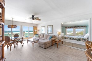 Uma sala de estar espaçosa com uma grande janela vista para o mar, um sofá confortável, uma mesa de jantar com cadeiras e uma pequena varanda.