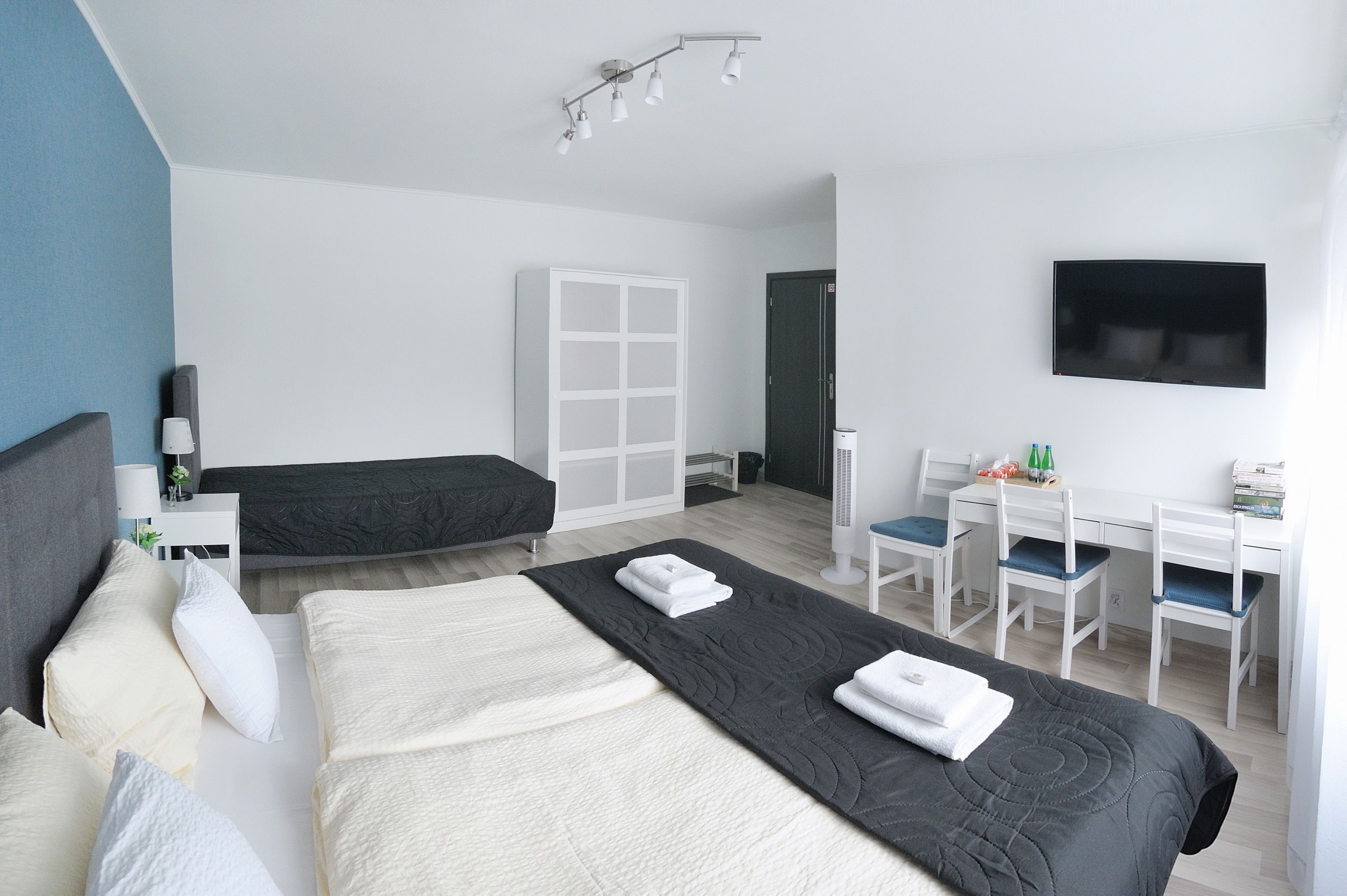 Une chambre d’hôtel moderne dotée d’un grand lit, d’un bureau avec deux chaises, d’une armoire et d’un téléviseur à écran plat fixé au mur.