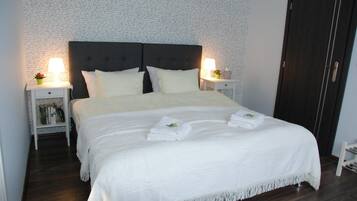 A neatly made bed with white linens and a dark headboard, flanked by bedside tables with lamps and small decorative items.