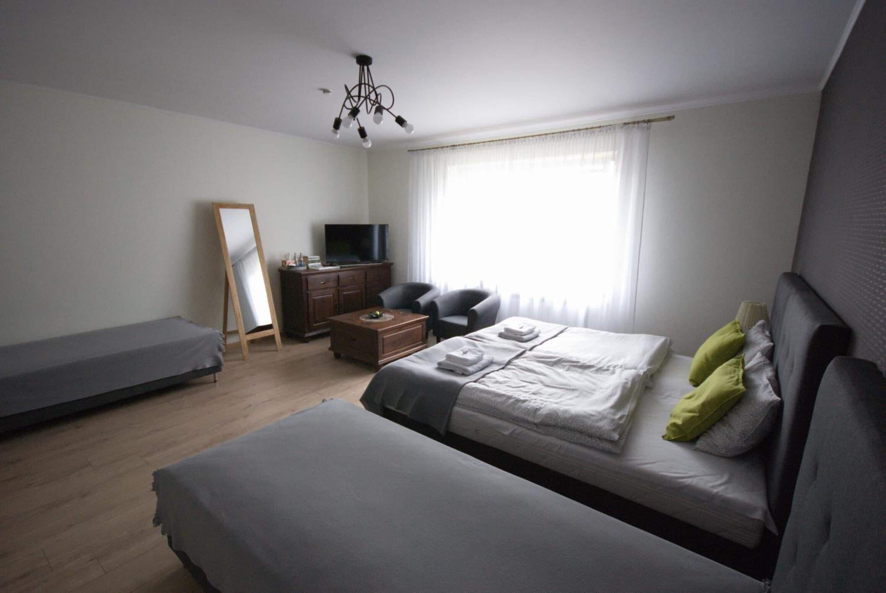 Un dormitorio moderno con una cama grande, una cama más pequeña, un escritorio, una silla, un televisor y un espejo.