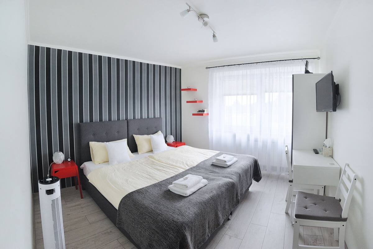 A modern bedroom with a large bed, bedside tables, a desk, and a TV.