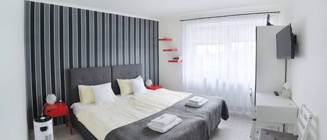 A modern bedroom with a large bed, bedside tables, a desk, and a TV.