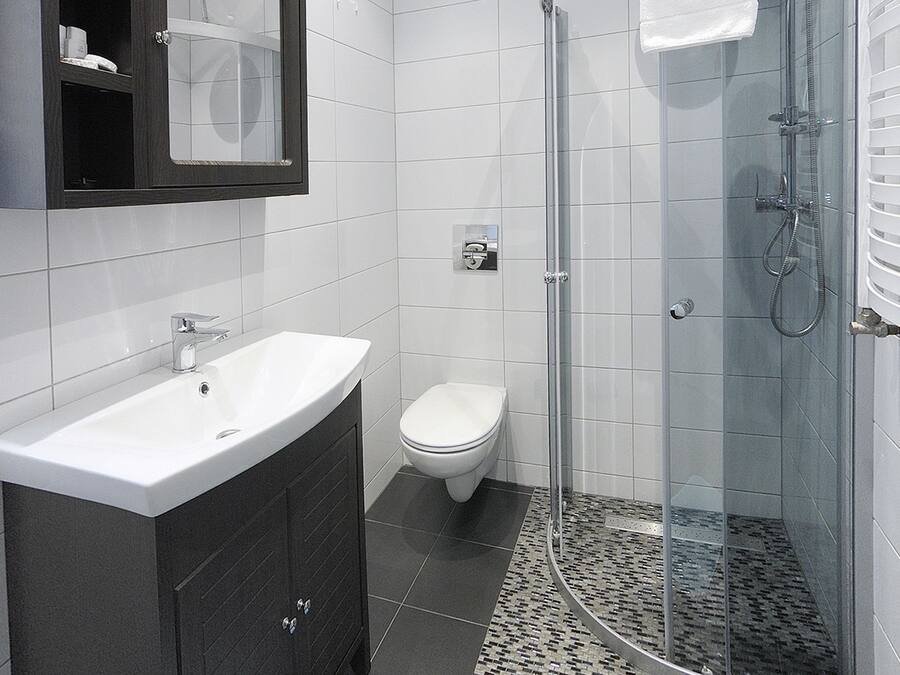 A modern bathroom with a white sink, dark cabinets, a glass shower enclosure, and a blue bath mat.