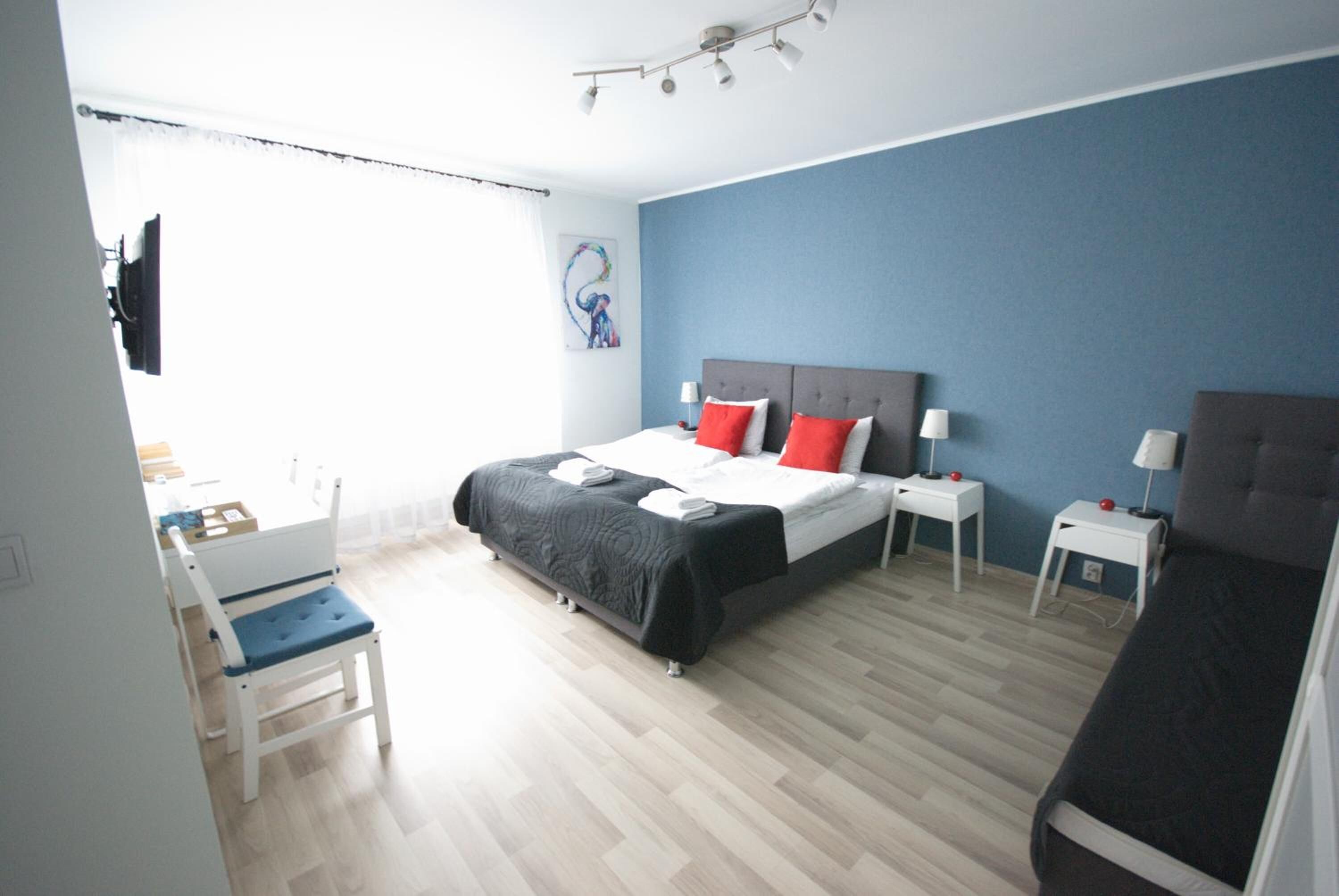 A hotel room with a bed, two bedside tables, a desk, a chair, and a window with curtains.