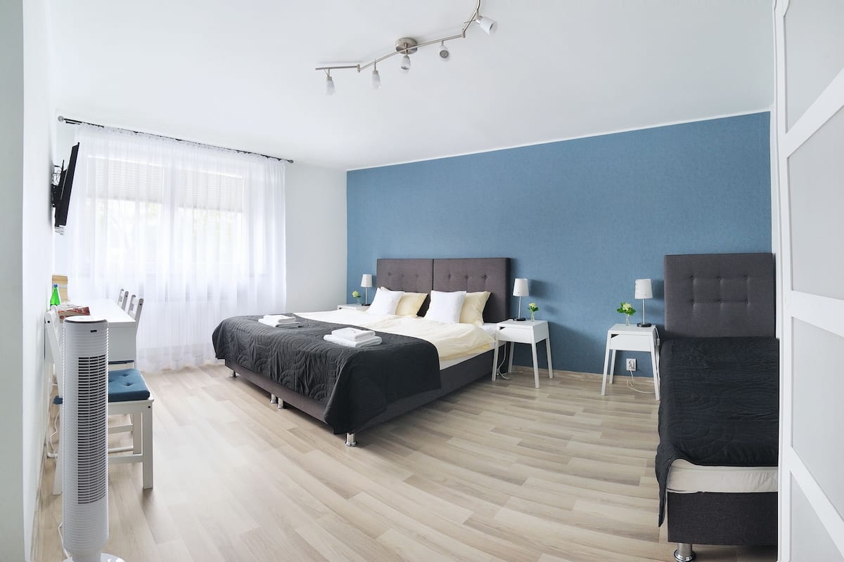 A modern hotel room with a bed, bedside tables, a desk, a chair, and a TV.