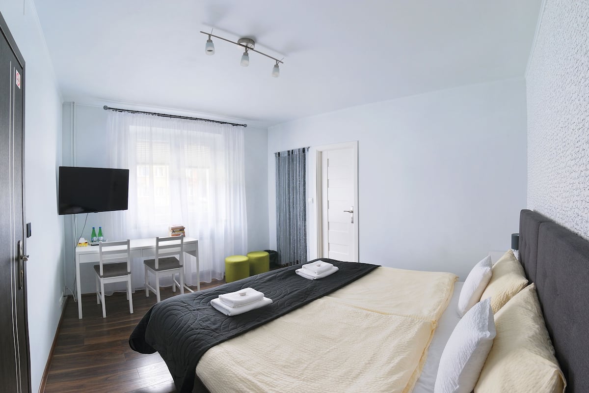 A hotel room with a bed, a desk with chairs, a television, and a door.
