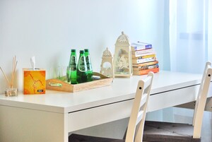 Uma mesa branca com um estojo de lenços de papel, garrafas verdes, copos, um suporte e uma pilha de livros.