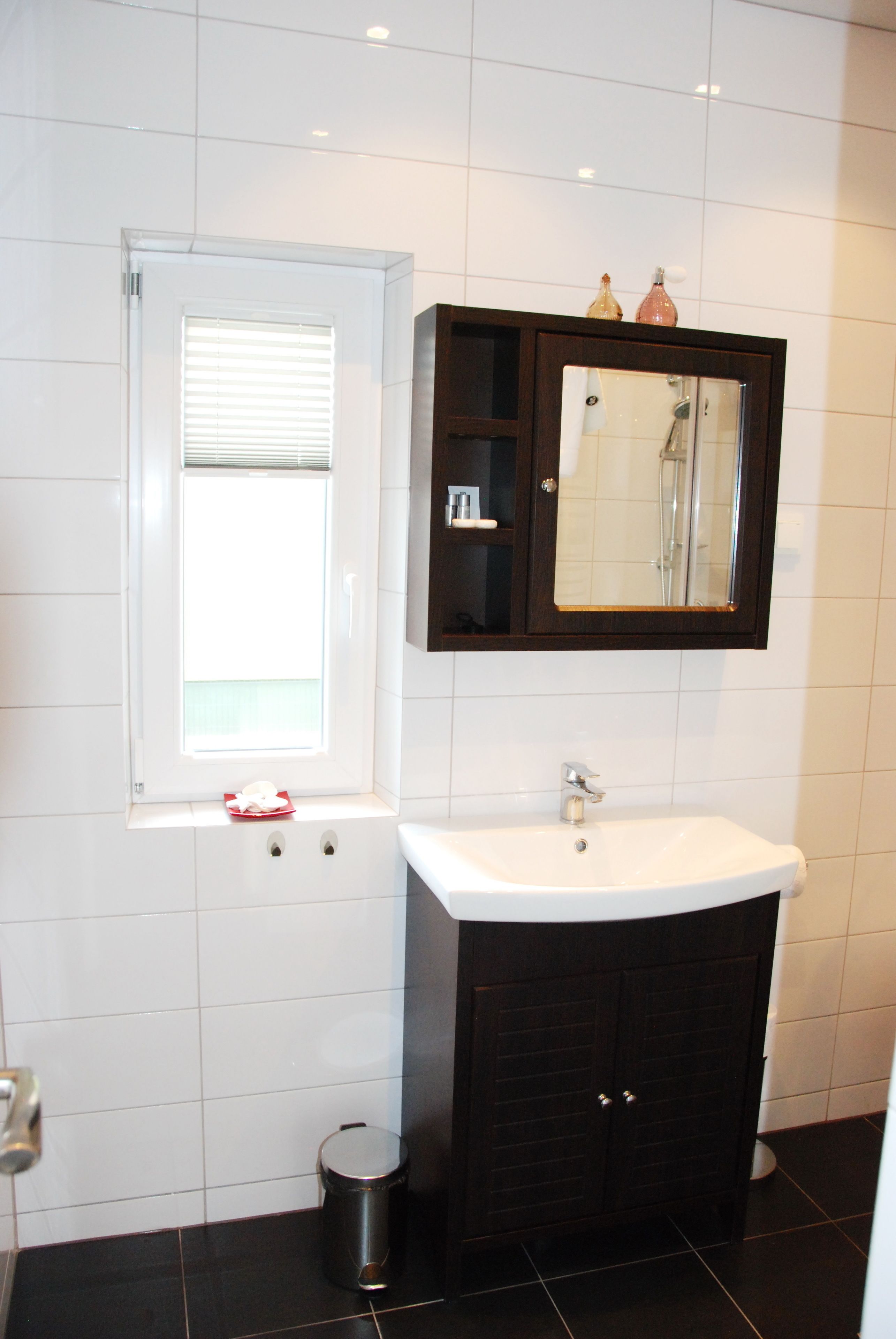 A bathroom with a white sink, dark cabinets, a window with blinds, and a mirror above the sink.