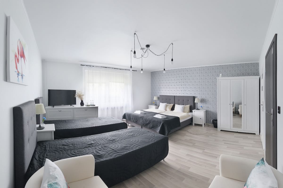 A modern hotel room with two beds, a television, a wardrobe, and a chandelier.