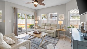 A living room with a ceiling fan, a sofa, a coffee table, and a television. - Pet-Friendly 3BR | Prime Beachwalk Location (Destin)