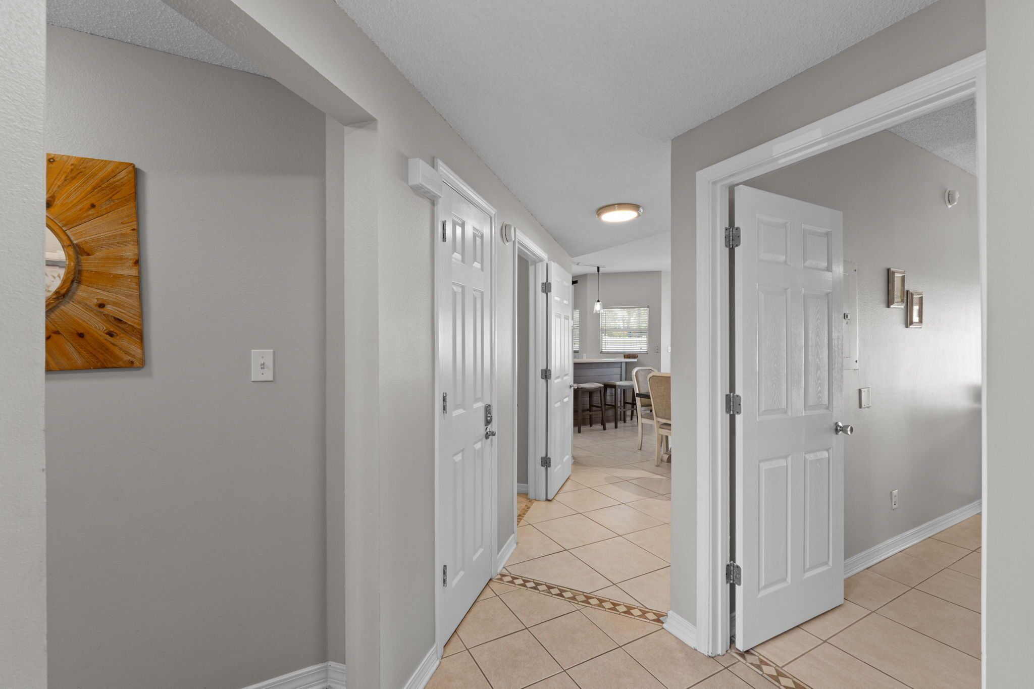 A hallway with white doors, a wooden wall art piece, and a dining area in the background.