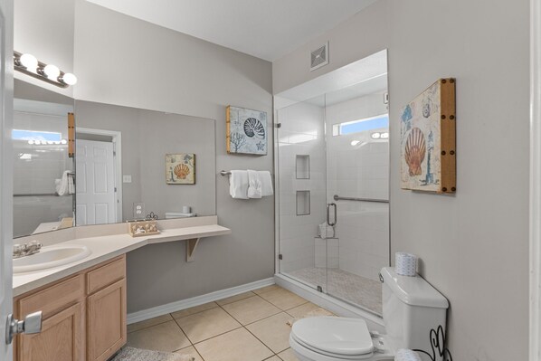 A bathroom with a sink, mirror, towel rack, toilet, shower, and decorative wall art. - Pet-Friendly 3BR | Prime Beachwalk Location (Destin)