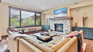A spacious living room with a stone fireplace, comfortable seating, and large windows.