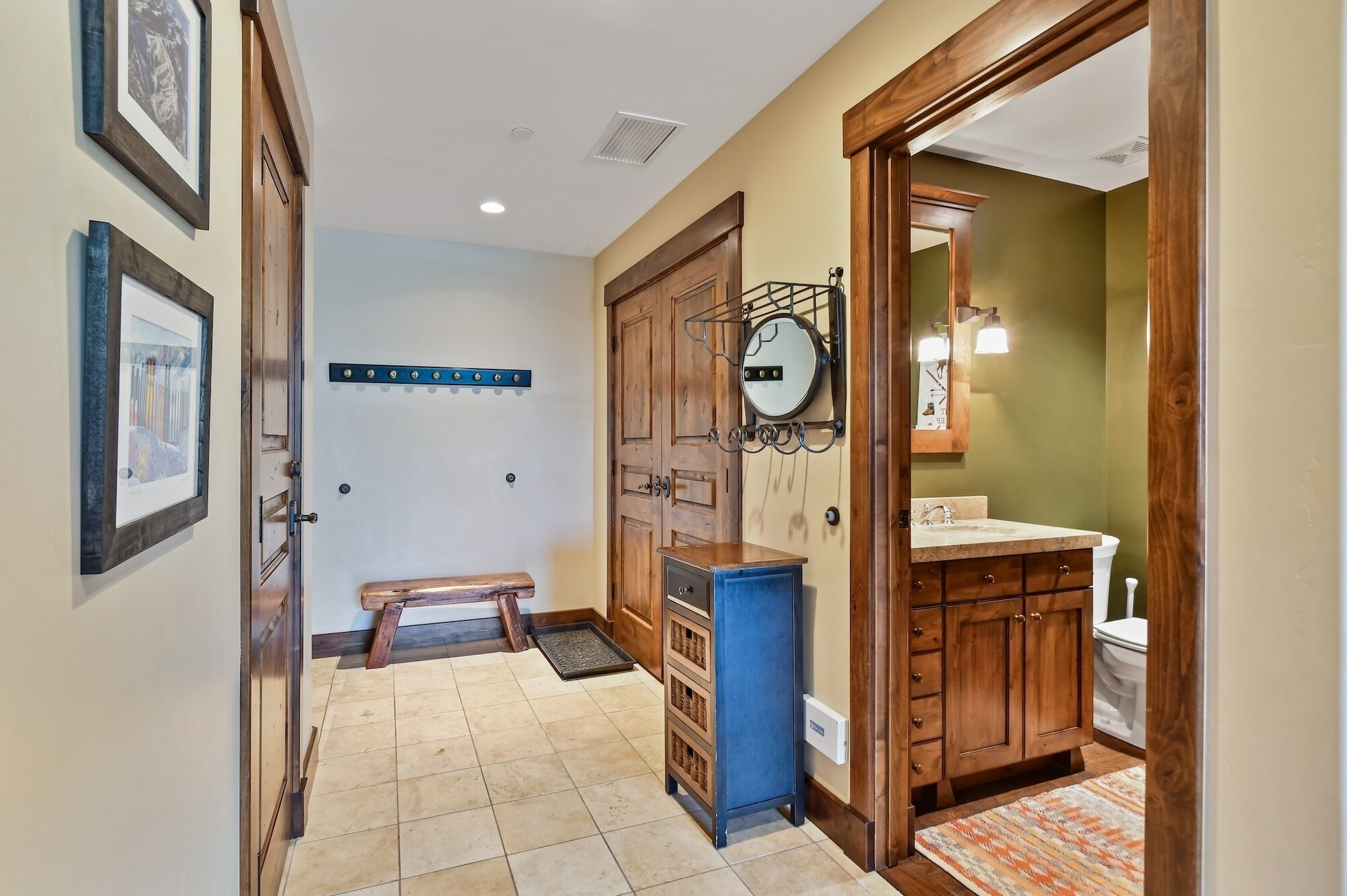 Un couloir avec un banc en bois, une porte avec un miroir et une salle de bain avec un lavabo et des toilettes.