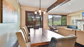 A dining area with a large wooden table, cushioned chairs, and a hanging light fixture.