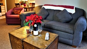 A living room with a grey sofa, a red armchair, a wooden coffee table with wine glasses and a bottle, and a remote control.