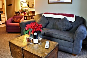 A living room with a grey sofa, a red armchair, a wooden coffee table with wine glasses and a bottle, and a remote control.