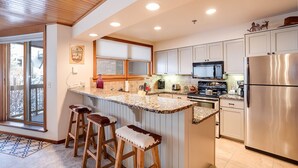 A modern kitchen with a central island, stainless steel appliances, and wooden bar stools.