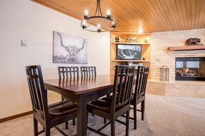 A dining area with a wooden table and chairs, a chandelier, a mounted TV, and a fireplace.