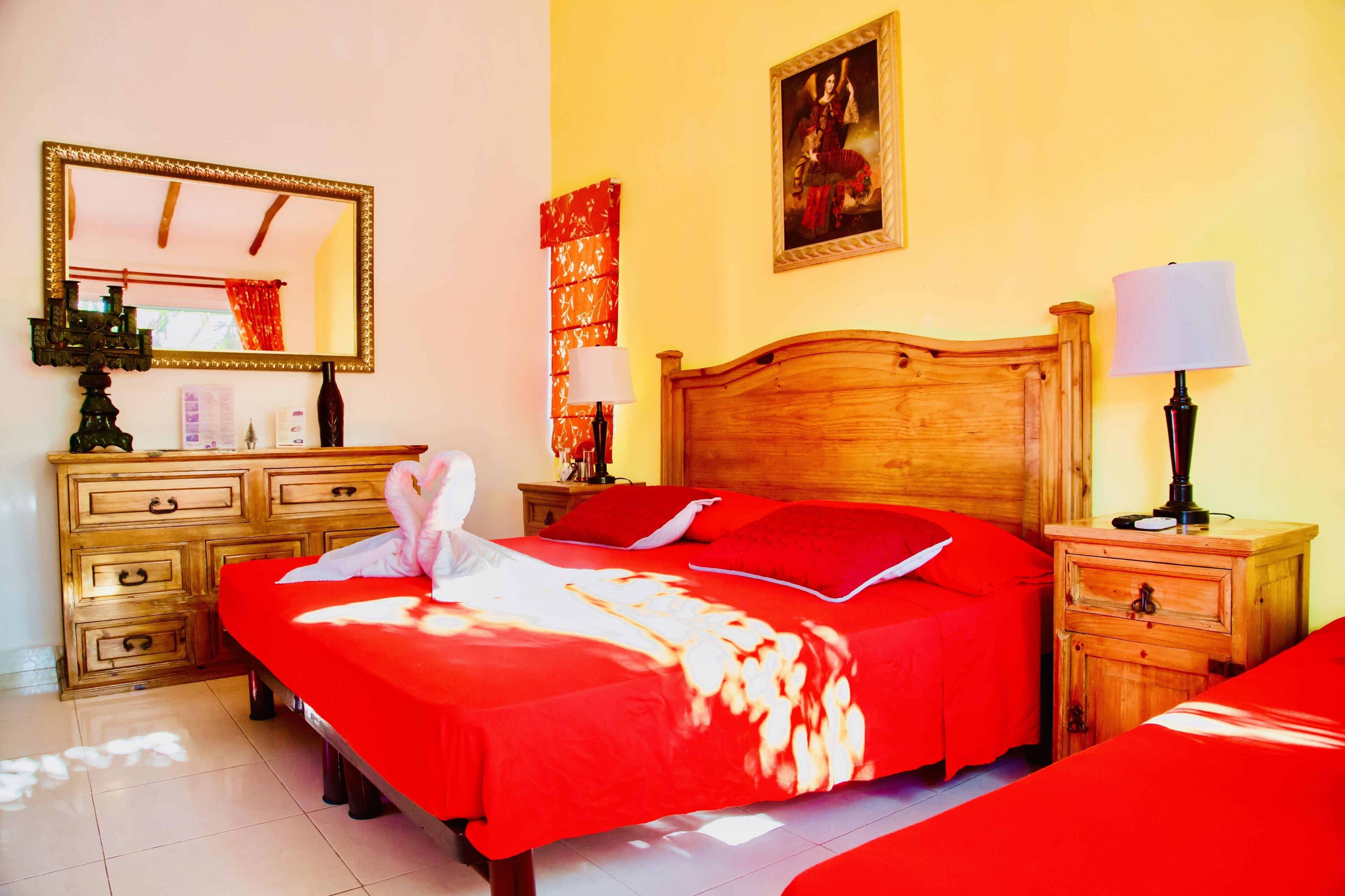 A hotel room with a wooden bed, a nightstand, a dresser, a mirror, and a painting on the wall.