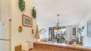 A kitchen with a granite countertop, a refrigerator, and a dining area with a table and chairs. - Fun island vibe! Private lanai, Full Kitchen, Flat Screen TV, Air Conditioning, WiFi- Kamaole Sands (KIHEI)