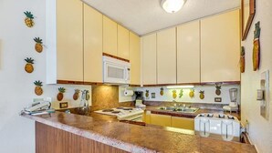 A compact kitchen with wooden cabinets, a granite countertop, a microwave, a stove, and a sink. - Fun island vibe! Private lanai, Full Kitchen, Flat Screen TV, Air Conditioning, WiFi- Kamaole Sands (KIHEI)