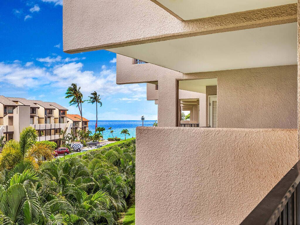A modern hotel with a balcony overlooking a lush garden and the ocean.