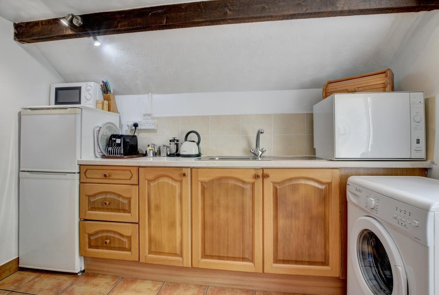 A compact kitchen with a refrigerator, microwave, kettle, sink, and washing machine.