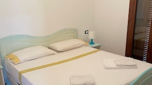 A bed with a headboard, a nightstand with a lamp, and a window with blinds. - Modern 1 bed apartment sleep 3 sea view only 700mt from sea (La Muddizza)