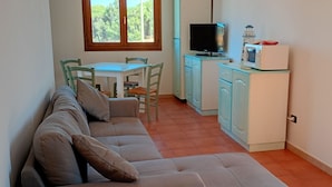 A compact living space with a sofa, a small dining table with chairs, a television, a microwave, and cabinets. - Modern 1 bed apartment sleep 3 sea view only 700mt from sea (La Muddizza)