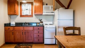 A kitchen with wooden cabinets, a stove, a microwave, and a refrigerator. - Alamo Springs- The Barn | Relaxing Retreat (Fredricksburg)