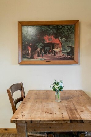 Une table à manger en bois, ornée d’un vase de fleurs, avec une chaise et un tableau encadré accroché au mur.