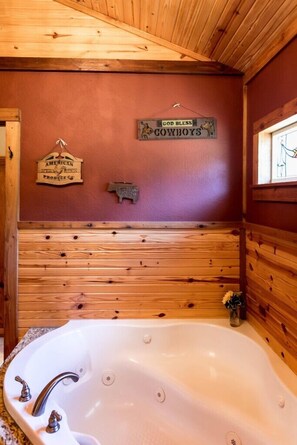 L’intérieur d’un chalet en bois, avec une grande baignoire, des murs en bois et une pancarte sur laquelle on peut lire : « Que Dieu bénisse les cow-boys ».