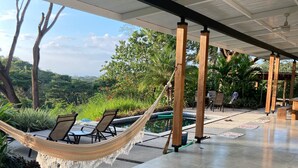 Un espacio al aire libre techado con una hamaca, sillas y una piscina.