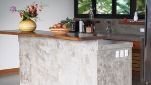 Una isla de cocina con encimera de hormigón, un florero con flores y un cuenco con fruta.