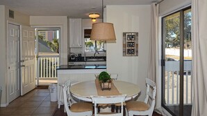 A dining area with a round table, chairs, a hanging lamp, and a view through a sliding glass door.