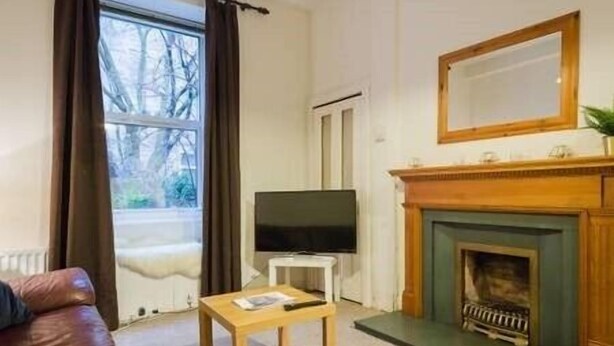 A living room with a fireplace, a television, and a window with curtains.